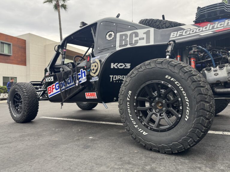 The BC-1 Baja Challenge vehicle sits parked on the pavement. It is black with multiple logos, including for BFGoodrich, Torque Wheels, SCORE, and KO3.